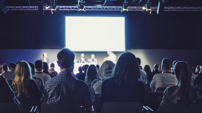 Uma audiência assiste a um painel em uma conferência.